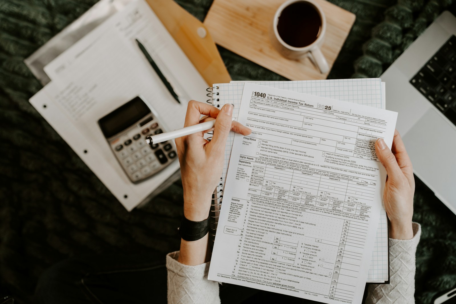 Person reviewing documents with calculator and laptop.